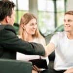 Dealership, the dealer is handing auto keys to a young couple, they are excited, cars standing in the background